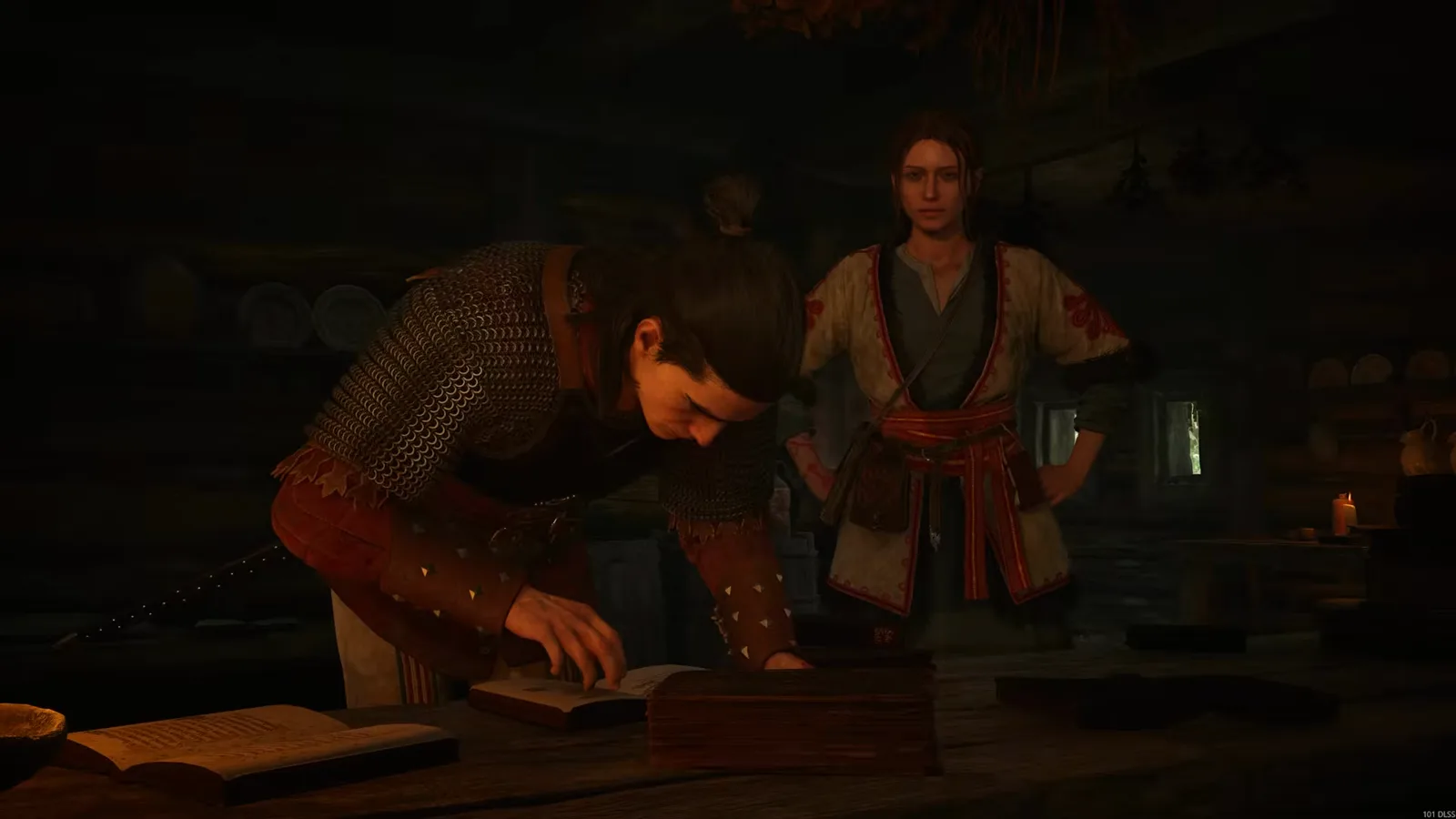 Coen leaning over an open book at a table while Anca, in her red-trimmed folk robe, watches from a candle-lit room during her companion quest in The Blood of Dawnwalker